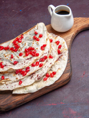 front-view-tasty-meat-qutabs-pitas-with-fresh-red-pomegranates-dark-purple-surface-meat-dough-pita
