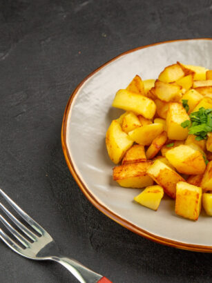 front-view-tasty-fried-potatoes-inside-plate-with-greens-dark-table