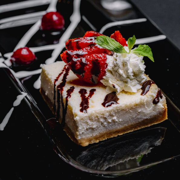 side-view-cheesecake-with-chocolate-whipped-cream-strawberry-mint-and-cherry-on-a-plate