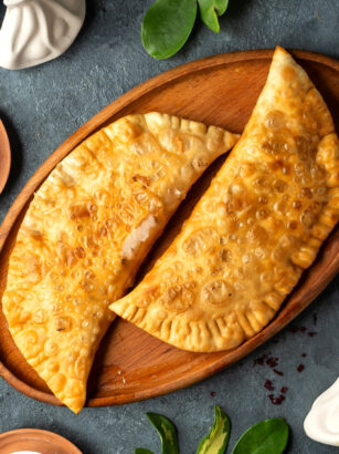 top-view-of-homemade-meat-pies-belyashi-on-a-wooden-platter-on-dark-background